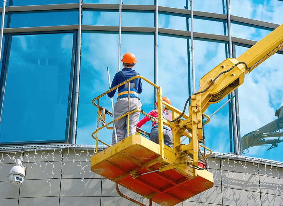 Fensterputzerin reinigt Glasfenster eines Gebäudes in der Höhe in einer Hebebühne. Arbeiter poliert Glas, Fensterputzen auf Bürogebäude im Kraneimer. Fensterputzer Außenglasfassade